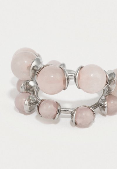 Strieborný prsteň s viacerými okrúhlymi svetloružovými kameňmi ruženínu osadenými okolo obvodu na bielom pozadí.