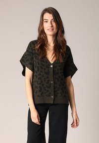 Cardigan à manches courtes, vert foncé avec un motif léopard. Fabriqué en matériau texturé, il présente des boutons sur le devant et un ourlet côtelé.
