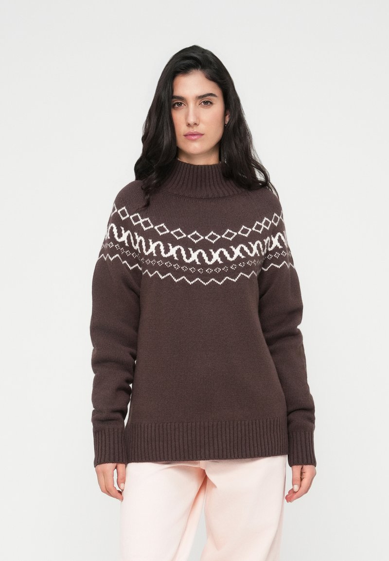 Καφέ πλεκτό πουλόβερ με ψηλό λαιμό και λευκό γεωμετρικό σχέδιο στο στήθος. Ριμπ μανσέτες και τελείωμα που δημιουργούν μια δομημένη εμφάνιση.