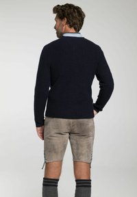 Marine ribbeltrui, gemaakt van een wolmix, met een getailleerd ontwerp; gecombineerd met lichtbruine shorts met zijveters en donkergrijze kniekousen.