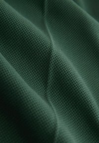 Tissu vert avec un motif texturé de maille gaufrée, présentant des plis doux et des ombres mettant en valeur la profondeur du matériau.