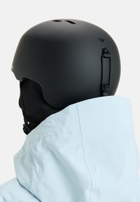 Zwarte ski-helm met ventilatiegaten, verstelbare band en matte afwerking, naast een kraag van een blauwe jas geplaatst.