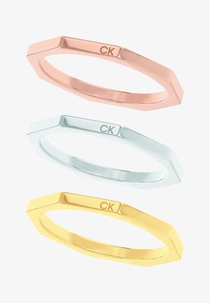 Zestaw trzech geometrycznych pierścionków w odcieniach różowego złota, srebra i złota. Każdy z nich ma polerowaną powierzchnię z subtelnym grawerunkiem "CK".