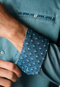 Cămașă cu un model albastru, realizată dintr-un material texturat cu un design geometric; gulerul prezintă un model de valuri albastre contrastante.