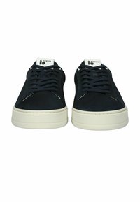 Zapatillas bajas negras para hombre con cordones negros, suelas gruesas blancas y etiquetas blancas en la lengüeta con la marca "BLCKSTN", vistas desde el frente.