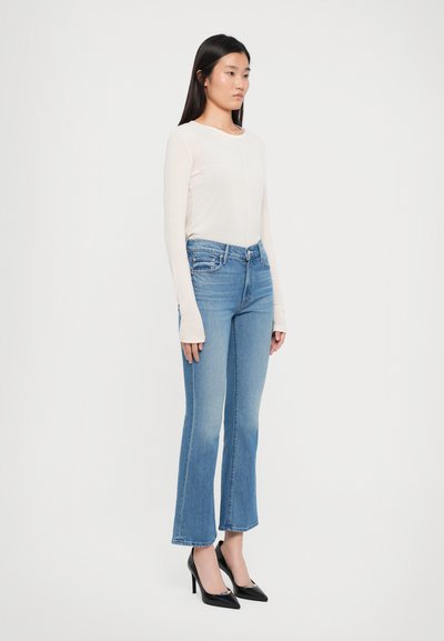 Lichtbeige langslijfs top gecombineerd met blauwe flared jeans. De jeans hebben een vervaagde textuur en een standaard tailleband. Zwarte hoge hakken.