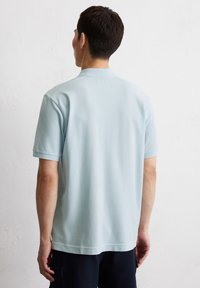 Helles blaues Polohemd mit kurzen Ärmeln aus weicher Baumwolle, ausgestattet mit einem klassischen Kragen und geradem Saum, Rückansicht zeigt minimale Markenkennzeichnung.