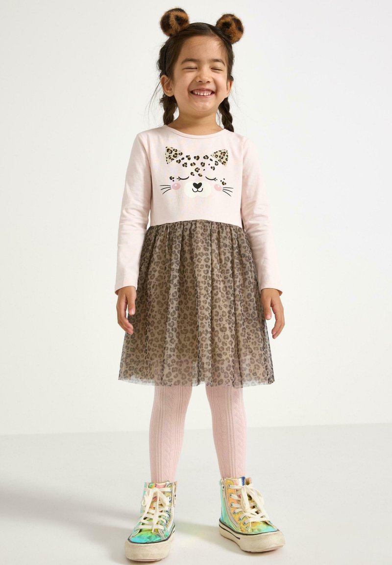Abito con stampa leopardata, con una maglietta a maniche lunghe rosa, gonna in tulle e orecchie di animale coordinate. Presenta sneakers colorate e lucide e collant rosa.