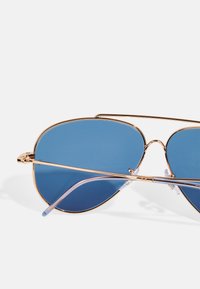 Ochelarii de soare de tip aviator au un cadru din metal auriu cu lentile albastre. Vârfurile transparente ale brațelor oferă confort. Finisaj neted, cu detalii hardware minime.