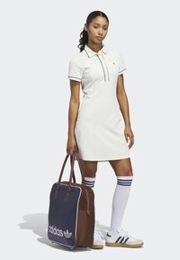 Weißes Polokleid mit schwarzer Paspelierung, kniehohe weiße Socken mit marineblauen Streifen, grün-weiße Turnschuhe und eine braun-blaue Umhängetasche.