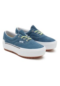 Zapatillas de ante azul con suelas de goma blanca, con cordones verdes y un diseño de perfil bajo. Superficie texturizada y detalle de raya negra en contraste.