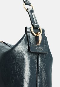 Marineblauwe leren handtas met een gestructureerde afwerking, goudkleurige hardware en een kenmerktag. De band heeft een strak ontwerp met een ringaccent.