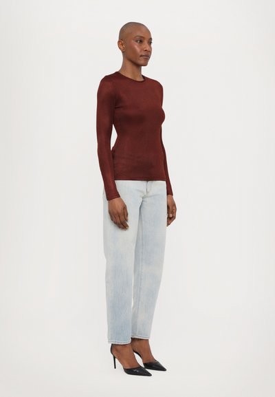 Enganliegender burgunderfarbener Langarmtop, kombiniert mit hellblauen Jeans im geraden Schnitt und schwarzen spitzen Pumps, die glatte Texturen und ein schlichtes Design zur Geltung bringen.