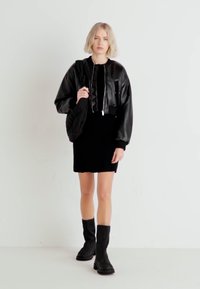 Black leather cropped jacket with a high collar, paired with a fitted black dress and knee-high black boots against a plain white background.