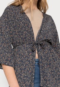 Navy Kimono mit floralem Muster und kurzen Ärmeln, ausgestattet mit einem Gürtel in der Taille und einem fließenden Design. Weicher Stoff mit leichtem Glanz.