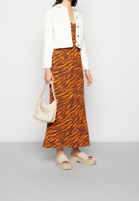 Robe rayée orange et marron façon tigre, associée à une veste courte blanche, un sac beige et des sandales à semelles épaisses beiges. Textures lisses, design décontracté.
