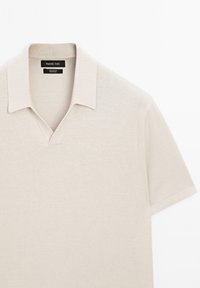 Polo a maniche corte beige con colletto aperto e una texture in maglia morbida, etichettato Massimo Dutti, realizzato in 100% cotone.