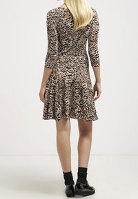 Sukienka w panterkę z dopasowanym górnym częścią, rozkloszowanym dołem, rękawami o długości czterech ćwiartek i miękkim materiałem. Czarne buty i skarpetki dopełniają stylizację.