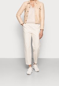 Ljust beige läderjacka med knapprad, ihop med en beige V-ringad tröja och krämfärgade avsmalnande byxor, samt vita sneakers.