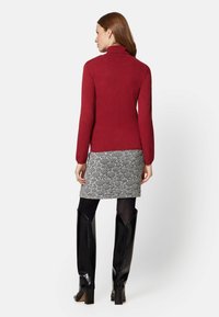 Red turtleneck sweater paired with a textured black and white skirt. The model wears shiny black knee-high boots.