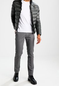 Grijze pufferjack met een glanzende afwerking, witte t-shirt, grijze slim-fit broek en zwarte veterschoenen. Eenvoudig ontwerp met horizontale stiksels.