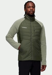 Roheline polsterdatud jakk kõrge kraega, fliisist varrukatega ja rinnaosal lukuga taskuga. Ees on brändi "Mammut" logo.