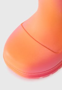 Botte en caoutchouc orange avec une texture lisse, un bout arrondi et une transition de couleur en dégradé vers le rose à la base. Présente un subtil détail de couture.