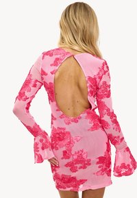 Vestido floral rosa con mangas largas, que presenta un escote en la espalda y puños acampanados. La tela es semitranslúcida con bordados florales en relieve.