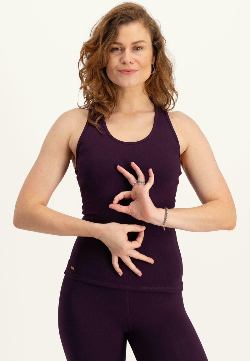 Lila linne i stretchigt tyg, med rundad halsringning och slim fit. Modellen visar handgester med en enkel design.