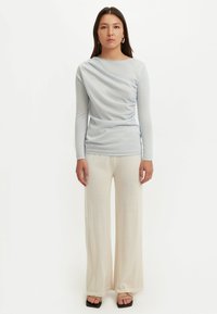 Hellblaues Langarmoberteil mit drapiertem Vorderteil, kombiniert mit cremefarbenen, weitem Bein-Hosen. Glatter, leichter Stoff mit entspannter Passform.