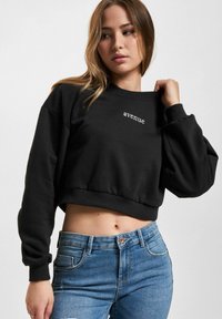 Svart cropped sweatshirt med "avenue" tekst i hvitt. Har ribbede mansjetter og hem, samt en myk stofftekstur. Brukt med blå jeans.