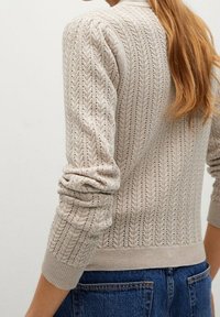 Vaaleanbeige neuletakki, jossa on teksturoitu siksak-kuvio, ribbineulotut hihansuut ja helma. Yhdistetty sinisiin farkkuihin.