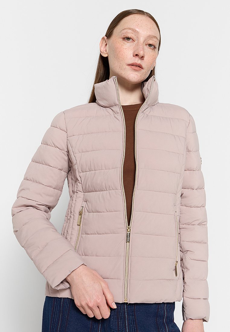 Giacca trapuntata rosa chiaro con colletto alto, dettagli in cerchio dorato e tasche laterali. Tessuto liscio e design aderente.