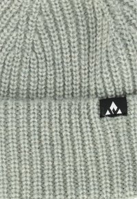 Ljusgrå stickad mössa med texturerad ribbmönster, med en svart etikett med en vit bergslogotyp på sidan.