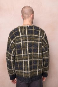 Tamsiai pilkas megztinis su žaliai ir baltais langeliais. Turi laisvą siluetą ir tekstūruotą medžiagą, su mentėmis ir apykakle, apipinta kraštu.