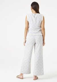 Lichtblauw en wit tweed set met mouwloze top en wijde broek. De top heeft franje randen, een keyhole detail aan de achterkant en een gestructureerde stof.