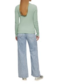 Hellgrünes langärmeliges Oberteil mit Struktur und figurschmeichelndem Design, kombiniert mit hellblauen weit geschnittenen Jeans und hellen Schuhen.