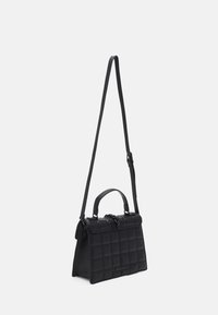 Mustaa suorakulmaista käsilaukua, jossa on tikattu kuvio, yläkahva ja pitkä säädettävä olkahihna valkoista taustaa vasten.