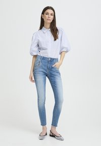 Jeans azzurri chiaro con vestibilità slim e orlo sfrangiato, abbinati a una camicia a righe bianche e blu con maniche a sbuffo e bottoni.