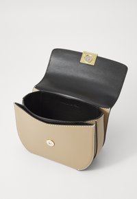 Borsa a tracolla in pelle khaki e nera con forma curva. Presenta una chiusura dorata, cuciture bianche e un compartimento interno vuoto.