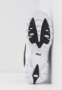 Suela de zapatilla en blanco y negro con una superficie de goma texturizada, que presenta un patrón ondulado y líneas de agarre prominentes. Logo de Fila visible.