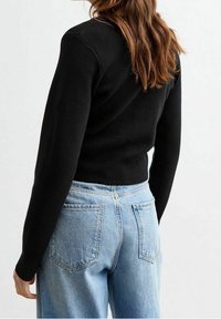 Schwarzer Strickpullover mit langen Ärmeln, gerippten Bündchen und Saum. Kombiniert mit hellblauen Jeans aus Denim mit zwei Gesäßtaschen.