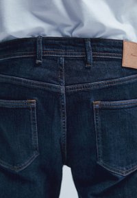 Mörkblå denimjeans med orange sömmar, synliga bakfickor och en tan-läderetikett på midjan. En enkel, klassisk design.