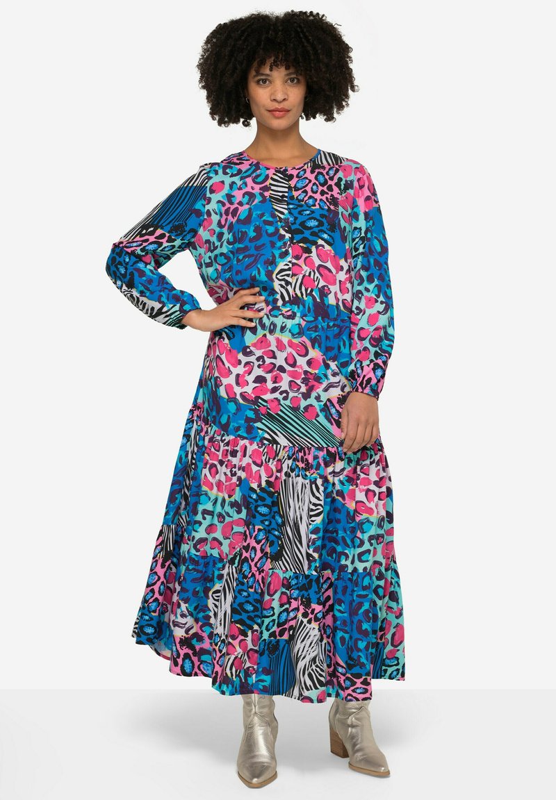 Robe maxi à manches longues et à volants dans un mélange vibrant de motifs, avec des nuances de bleu, de rose et des rayures zèbres noir et blanc. Texture soyeuse.
