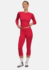 Rode sportieve top met lange mouwen, voorzien van een getailleerd ontwerp en textuuraccenten, gecombineerd met bijpassende geknipte leggings; zacht materiaal.