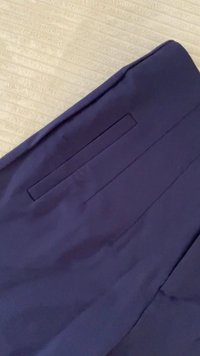 Calças ajustadas azul-marinho, feitas de tecido suave, com um bolso decorativo e vincos acentuados ao longo das pernas.
