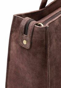 Bruine suede handtas met een ritsluiting, platte handvatten, messingen hardware en een zachte, gestructureerde oppervlakte met nette randen.