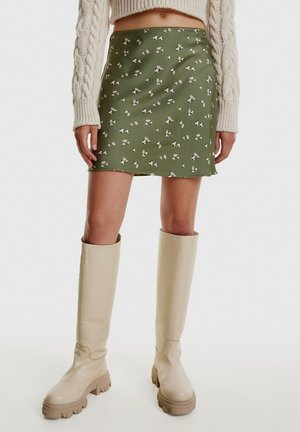 Groene bloemenrok met een gladde textuur, versierd met kleine witte bloemen. Gecombineerd met beige kniehoge laarzen met dikke zolen.