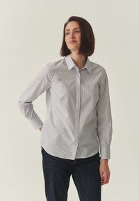 Chemise boutonnée en tissu léger à rayures verticales bleues et blanches. Elle comporte des manches longues, un col classique et un ourlet arrondi.