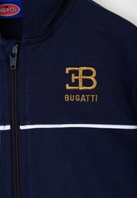 Giacca a zip navy con strisce bianche, logo dorato ricamato "EB" e testo "BUGATTI" sottostante. Realizzata in un tessuto morbido con una texture liscia.